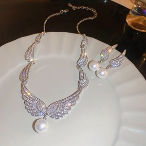 Detail shot of silver wing-shaped zircon necklace and pearl earrings on ceramic plate