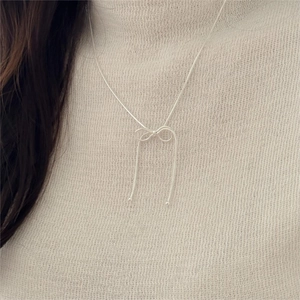 Detail of silver bow pendant on snakeskin chain worn over beige knitwear