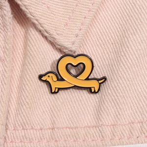 Detail einer gelben herzförmigen Dackel-Emaille-Anstecknadel auf rosa Jeansstoff
