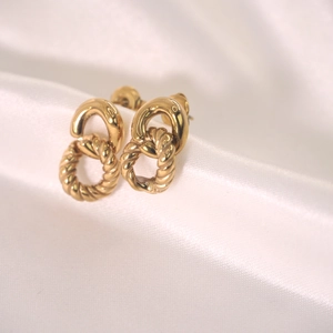 Twisted gold hoop earrings made of stainless steel displayed on a white silk background
