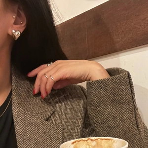 Close-up of minimalist silver heart studs and simple stackable rings worn on hand