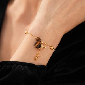 Detail von Tigerauge-Armband mit goldenem Kürbis und Münzanhängern am Handgelenk