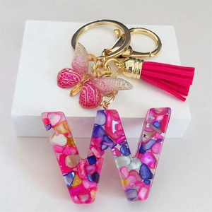 Detail of resin letter W keychain with pink butterfly, rose red tassel and gold clasp