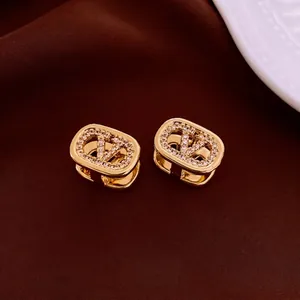 18k gold plated oval huggie earrings with V-shaped crystal logo on silk background