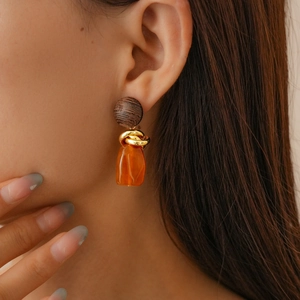 Detail of vintage resin geometric earring with brown wood texture and golden twist ring