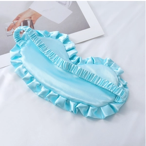 Nahaufnahme einer hellblauen Satin-Schlafmaske mit Rüschenrand und Gummiband auf weißem Stoff