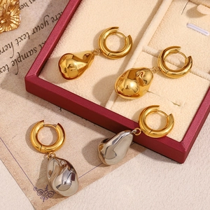 Macro detail of teardrop liquid metal earrings in gold and silver finish on a gift box