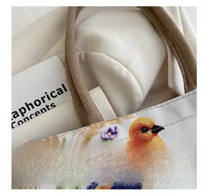 Close-up of high-density colorful bird embroidery on a minimalist beige canvas tote bag