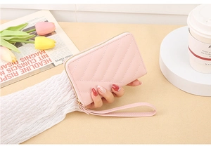 Pink V-quilted faux leather zip wallet with wrist strap held against a lifestyle background