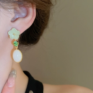 Detail shot of elegant floral earrings with green resin petals and white jade-like drop
