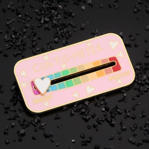 Macro detail of interactive pink enamel pin with sliding metal heart gauge on black stones