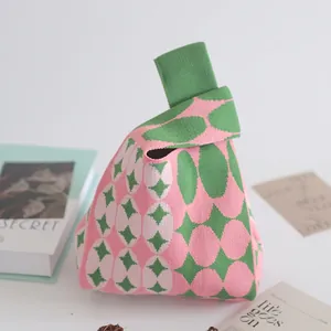 Pink and green knitted bucket bag with geometric patterns on a clean white desk