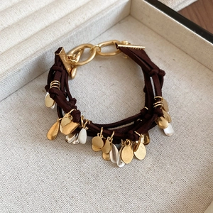 Detail of dark brown leather multilayer bracelet with gold and silver charms in a linen box