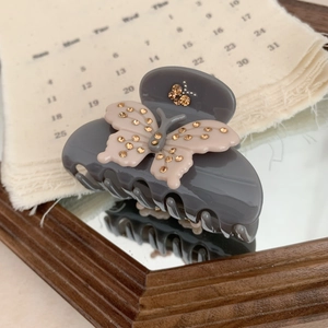 Detail of grey hair claw clip with pink rhinestone butterfly on a mirror surface