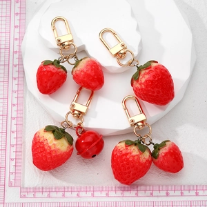 Handmade resin strawberry keychains with red bells on a white stone display tray