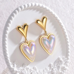 Detail of elegant gold heart earrings with iridescent pearl texture on ceramic tray