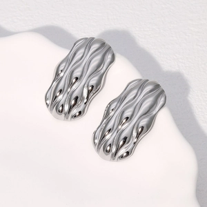 Macro shot of silver wave textured stainless steel earrings on a white ceramic tray