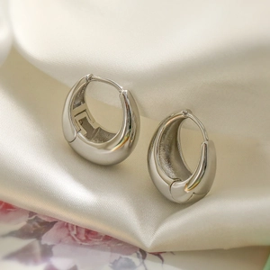 Polished silver geometric hoop earrings on soft white silk background with floral detail