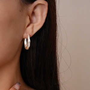 Macro shot of silver metallic hoop earrings with irregular wave design worn by model