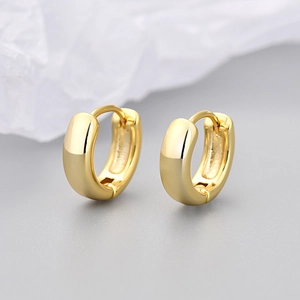 Polished gold huggie hoop earrings on a textured paper surface in a macro detail shot