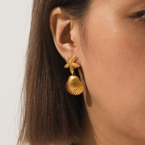 Detailed view of elegant gold starfish and seashell earrings worn by a model