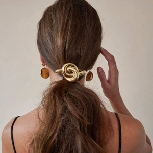 Elegant gold-tone knot hair clip on a low ponytail featuring a polished mirror finish
