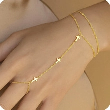 Détail macro d'un bracelet de main doré avec croix pour femme porté par un mannequin