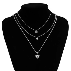 Close-up of triple-layered silver necklace with heart and disc pendants on model