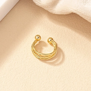Detailed view of a multi-layer gold ear cuff with spherical ends on a soft textured background