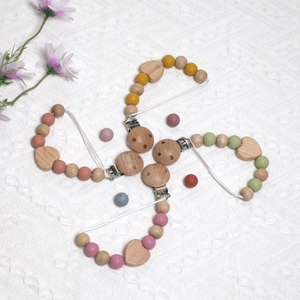 Flat lay of colorful silicone pacifier clips with beech wood heart beads and metal clips