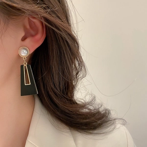 Close-up of geometric earrings featuring black trapezoid drop and faux pearl stud on model