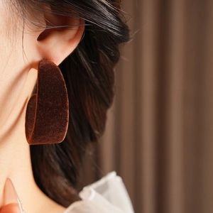 Close-up of a wide C-shaped dark brown velvet hoop earring on a model ear