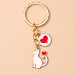 Close-up of golden keychain featuring white enamel cat and red heart charm pendants