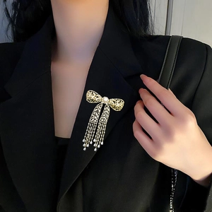 Detail einer eleganten Brosche mit Schleife, Quasten und Perle auf schwarzem Anzugrevers