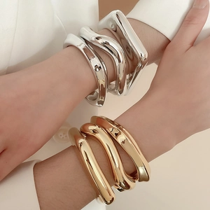 Detail of irregular geometric wave cuffs in polished silver and gold on model wrist