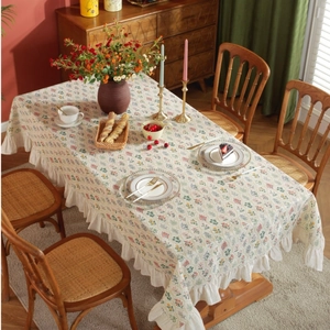 Detailed close-up of pastoral floral tablecloth with ruffled edges on a wooden table