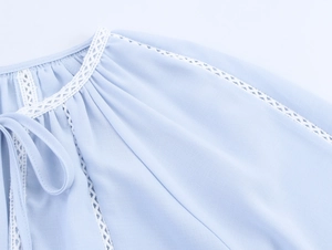 Detail of light blue shirt featuring white lace stitching and adjustable neck tie ties