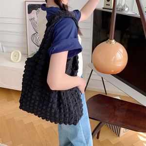 Side view of a large black tote bag with quilted bubble texture worn by a model
