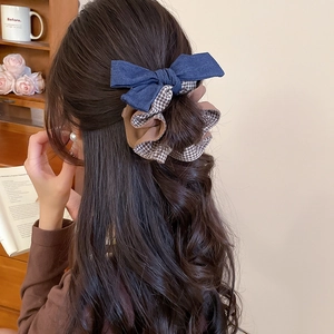 Rear view of a model wearing a large plaid bow scrunchie in a cozy vintage room