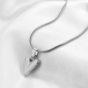 Detail of polished silver heart pendant necklace on soft white silk fabric background