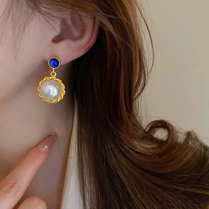 Detail of vintage gold-rimmed pearl earring with blue gemstone accent on a model