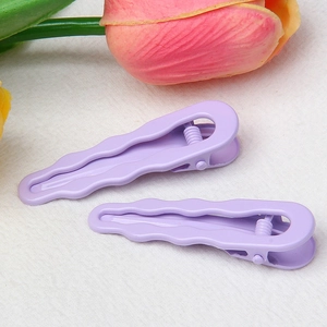 Detail view of two lavender purple wave-shaped hair clips on white fabric with tulips