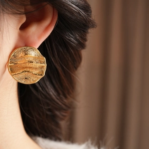 Vue détaillée de grandes boucles d'oreilles rondes dorées avec finition martelée sur modèle