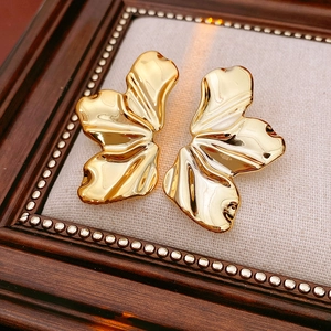 Detail shot of golden textured leaf earrings on an elegant fabric background inside a frame