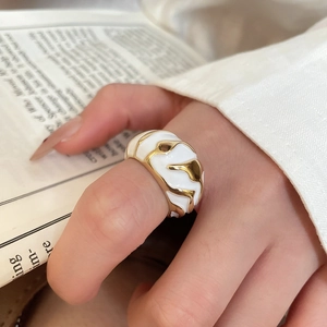Detail of irregular wave-shaped gold ring with white enamel finish on a book