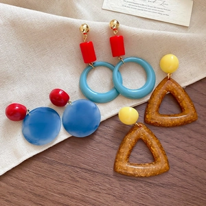 Detailed flat lay of colorful geometric resin drop earrings on a rustic wood and linen surface