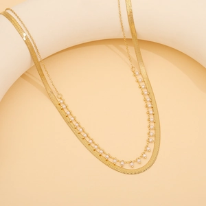Detail einer goldfarbenen zweilagigen Halskette mit Schlangenkette und Perlen