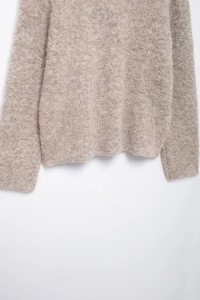 Nahaufnahme der flauschigen Textur und Strickbündchen an der beigen Strickjacke