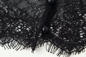 Close-up of intricate black lace texture and decorative pearl buttons on the dress