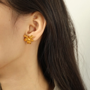 Polished gold flower stud earrings in a minimalist six-petal design worn on model